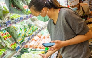 A woman is picking vegetable wrapped in plastic in a supermarket isle.